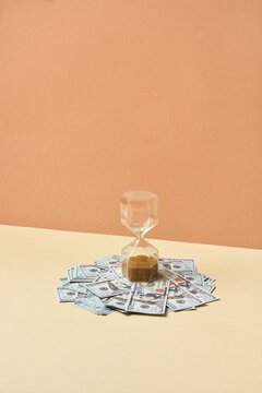 Vintage hourglass placed on pile of dollar bills.