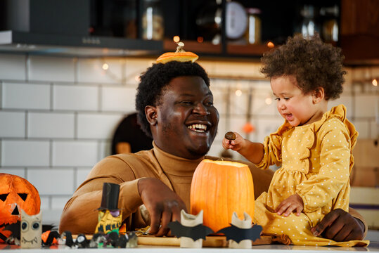 Father and cute little daughter having fun with jack -o -lantern in the kitchen. Halloween holiday