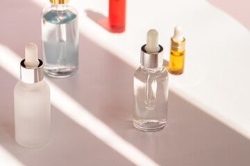 Different glass dropper bottles with face serum, natural oil and anti-age moisturizer in sunny room. Skincare, facial and body cosmetics concept. High contrast photo, front view
