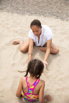 Teen girl making a mermaid tail out of sand for her sister