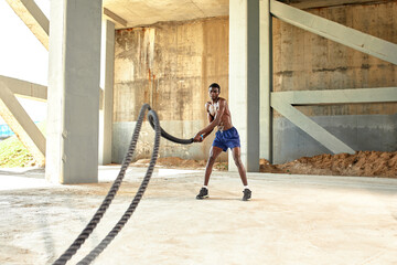 Rope workout. Sport man doing battle ropes exercise outdoor. Black male athlete exercising, doing functional fitness training with heavy rope