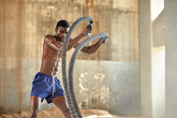 Rope workout. Sport man doing battle ropes exercise outdoor. Black male athlete exercising, doing...