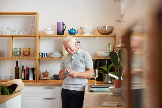 Happy Elderly Man Using Smartphone In Kitchen