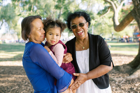 Two grandmothers hugging and laughing with granddaughter together