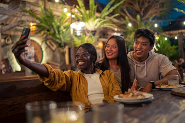 Small multiethnic group of friends taking selfie at dinner table