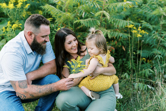 Parents smiling while holding their toddler daughter in yellow romper