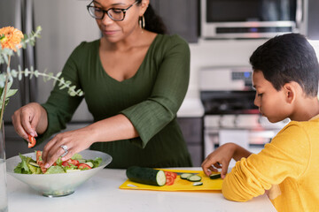 Mother preparing salad with her son while eats cucumber