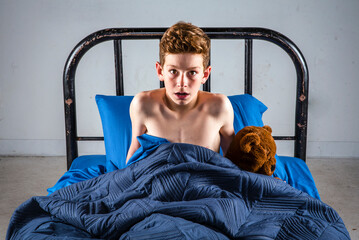 Startled boy sitting up suddenly in bed after hearing a scary sound
