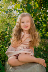 Adorable little child girl in beautiful dress sits on the big stone and smiles on the farm. Girl in the summer garden. Summer season.