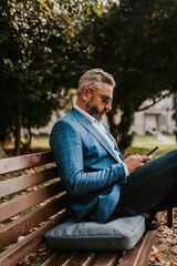 Obraz premium Modern senior businessman using smartphone for online meeting while sitting on bench