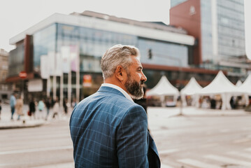 A senior businessman in a suit walking around the city after work