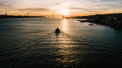 Wake of nautical vessel at sunset on Tagus River in Lisbon, Portugal with 25 April Bridge in the background