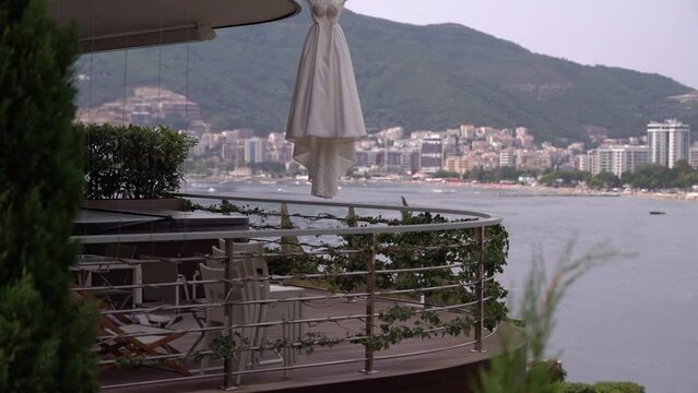 White wedding dress with a long train hangs on a hanger on the balcony of an expensive hotel