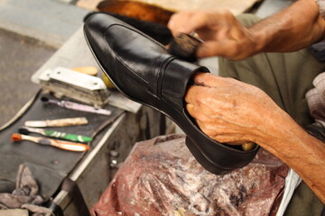 An old man hand polishing and painting a black shoe at stall