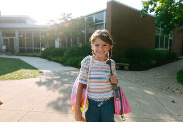 Young girl smiles at the camera in front of her school