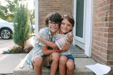 Siblings hugging on front step of home