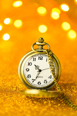 Christmas wallpaper. Golden watch in gold glitter on a yellow background with shining bokeh.holiday time.Holiday lights.Beautiful Christmas background in warm golden colors.