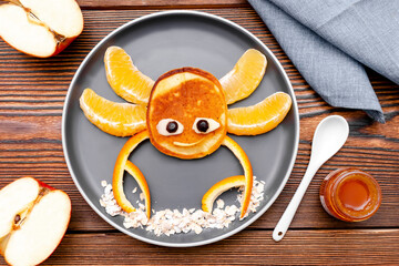 Funny crab face shape snack from pancake, orange,apples,honey on plate. Cute kids childrens baby's sweet dessert, healthy breakfast,lunch, food art on wooden background,top view