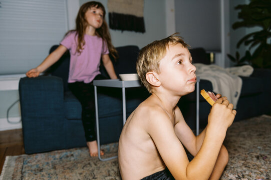 Two children in living room watching TV and eating food