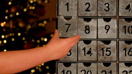 Christmas time.advent calendar. child hand opens the advent calendar near Christmas tree with glowing garland near Christmas tree with glowing garland.Gifts and surprises for Christmas and New Year. 
