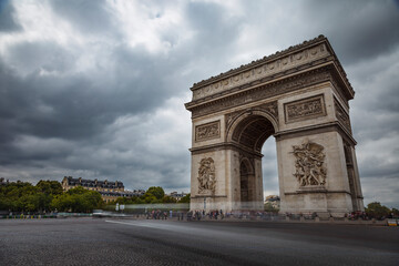 Fototapeta na wymiar Arc de Triomphe at dramatic sky with storm clouds and blurred car, Paris, France