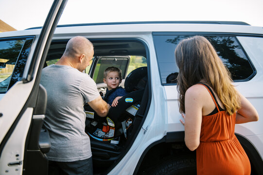 Smiling Father Putting His Toddler Son Inside Car Seat