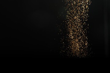 Shiny golden glitter falling down on black background, space for text. Bokeh effect