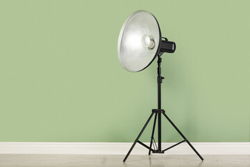 Professional beauty dish reflector on tripod near pale green wall in room, space for text....