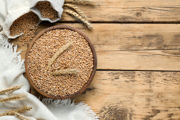 Bowl of wheat grains and spikes on wooden table, flat lay. Space for text