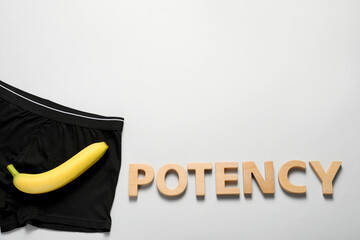 Men underwear with banana and word Potency made of wooden letters on light grey background, flat...