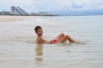 A smiling boy bathes in the sea against the backdrop of coastal hotels in Vietnam.