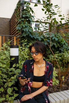 Asian freelancer using devices on bench in a garden 