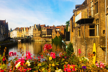 Fototapeta na wymiar Scenic cityscape of Ghent with traditional Flemish style brick townhouses decorated with colorful blooming flowers on banks of Leie river on sunny summer day, Belgium.
