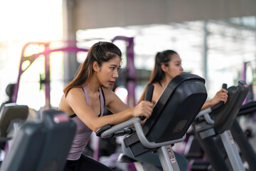 Fototapeta na wymiar Side shot of attractive woman at the gym riding on the spinning bike with copy space, sporty asian woman riding an exercise bike