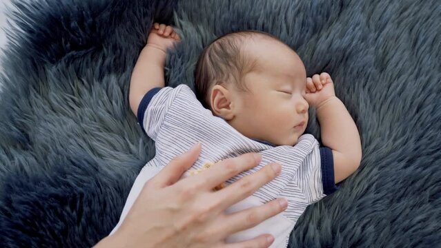 0-1 month Asian newborn boy sleep on blue cotton fur happy and tender, mother hand put on infant's chest to protect or prevent flinch or appalled while toddler sleeping, hospitality motherhood concept