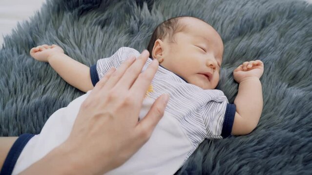 0-1 month Asian newborn boy sleep on blue cotton fur happy and tender, mother hand put on infant's chest to protect or prevent flinch or appalled while toddler sleeping, hospitality motherhood concept