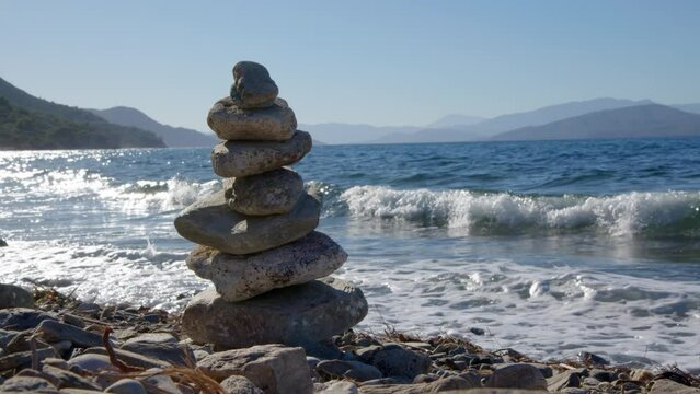 Stones lie on top of each other in balance on stone beach with sea or ocean with waves in background. concept of calmness and patience, feng shui near pond. pyramid of stones stacked.