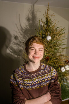 A smiling red-haired guy in a Christmas sweater with a dried spruce