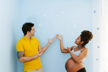 Smiling pregnant multiracial couple standing over blue backgroun