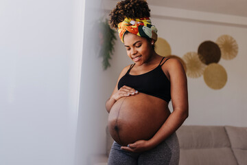 Happy pregnant woman touching her belly at home