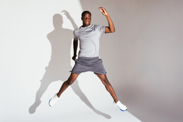 Black sportsman jumping against gray backdrop