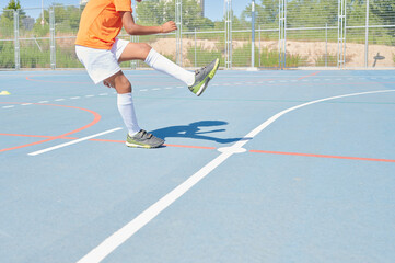 Fototapeta premium Unrecognizable young boy with Netherlands national football team equipment playing football in a training field. Learn to strike.