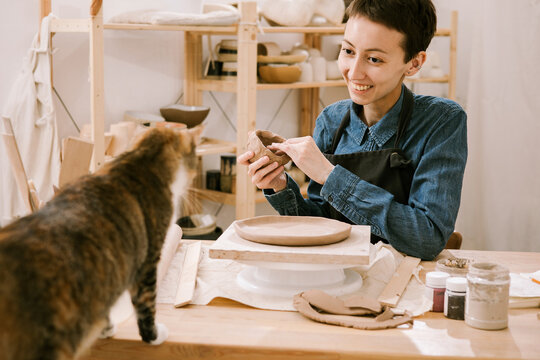 Young woman smiling at her cat while sculpting clay