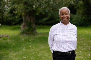 Mature, smiling black woman with dreadlocks outside in nature.