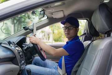 Asian male driver in a blue shirt, hat, glasses, driving a car