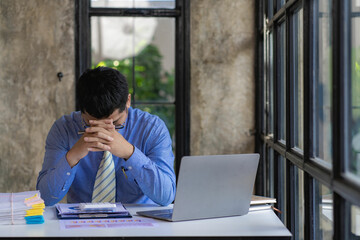 A young Asian businessman has a headache and eyestrain while working on a laptop from overtime.