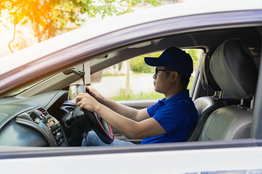 Asian male driver in a blue shirt, hat, glasses, driving a car