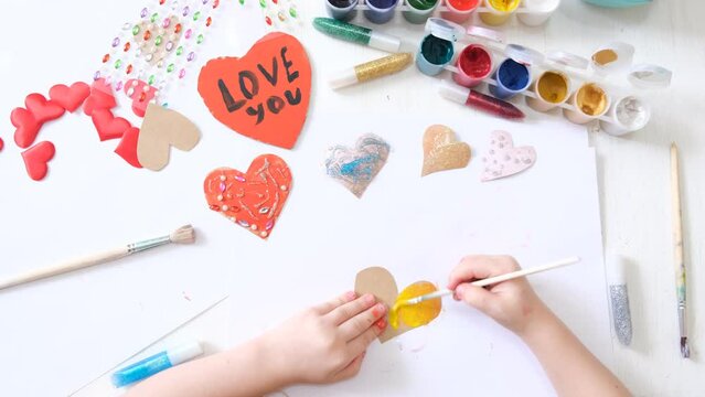 Child making homemade greeting card.  Toddler girl coloring  hearts  for Mothers Day, Fathers day or Valentines day . 