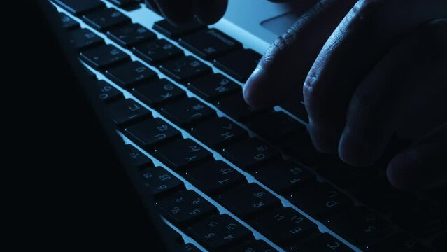 暗い部屋でパソコンを操作してキーボードで入力作業している男性の手
