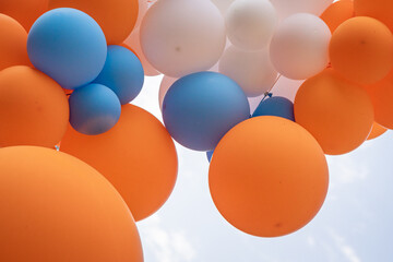 Multicolored set of balloons in front of the blue Autumn sky. Orange, white and blue balloons.